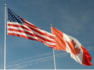 Canadian and US flags on poles. The background is a blue sky.
