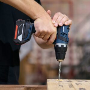 A person using a power drill to drill a hole in a plank of wood.