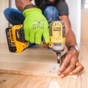 A man is using a yellow impact driver to attach a metal bracket to a piece of wood.