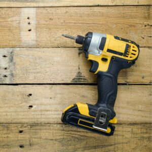 A yellow and black impact driver lying on its side on some planks of wood.