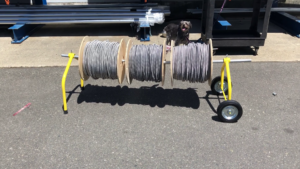The Big E-Z wire spool rack from Rack-A-Tiers. It is dispensing 3 spools of metallic cable.