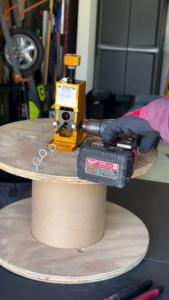 rack-a-tiers wire peeler copper wire stripper mounted to a wooden cable spool. an electrician has attached a milwaukee drill to the wire peeler