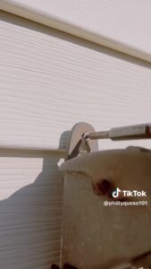 a square head drill bit removing a screw from the panel siding of a house