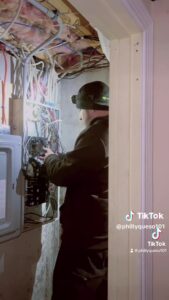 An electrician wiring a residential panel. the electrician is wearing black clothes.